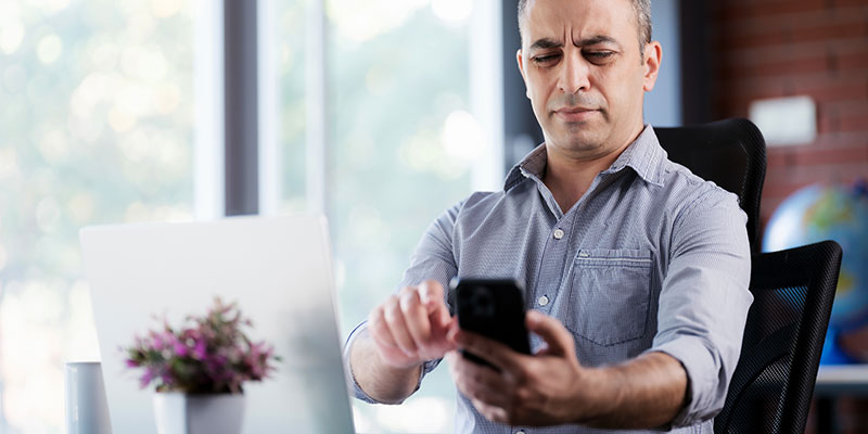 hombre aleja su telefono para aliviar la fatiga visual