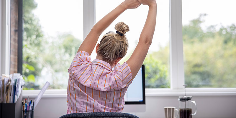 mujer en oficina estirandose frente a la computadora