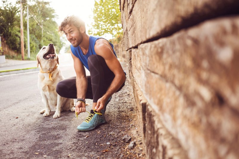 Hombre atándose los cordones de sus zapatillas con su perro al lado.