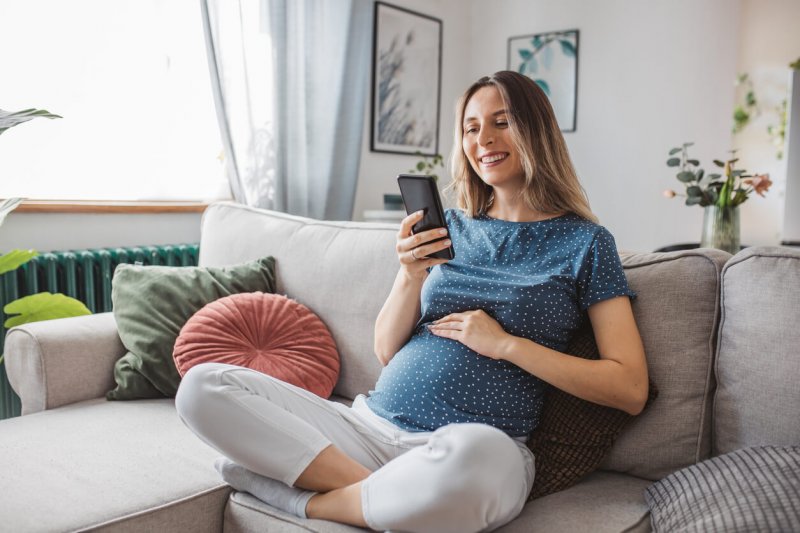 mujer embarazada sentada en un sillón revisando su celular